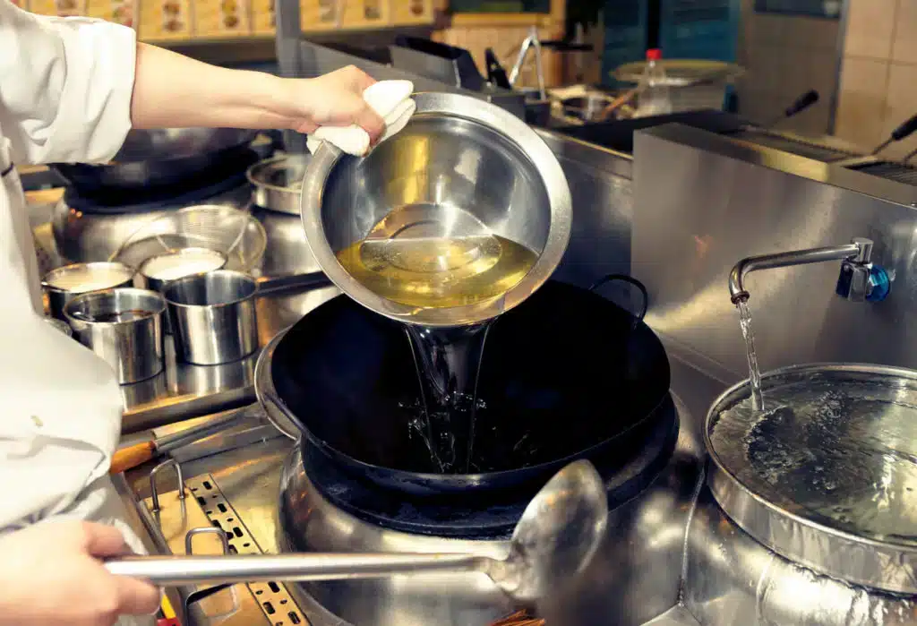 Commercial kitchen chef cooking with oil in a frying pan
