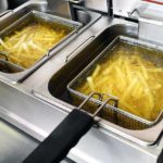 French fries or potato chips deep frying in oil in a commercial metal fryer in a restaurant
