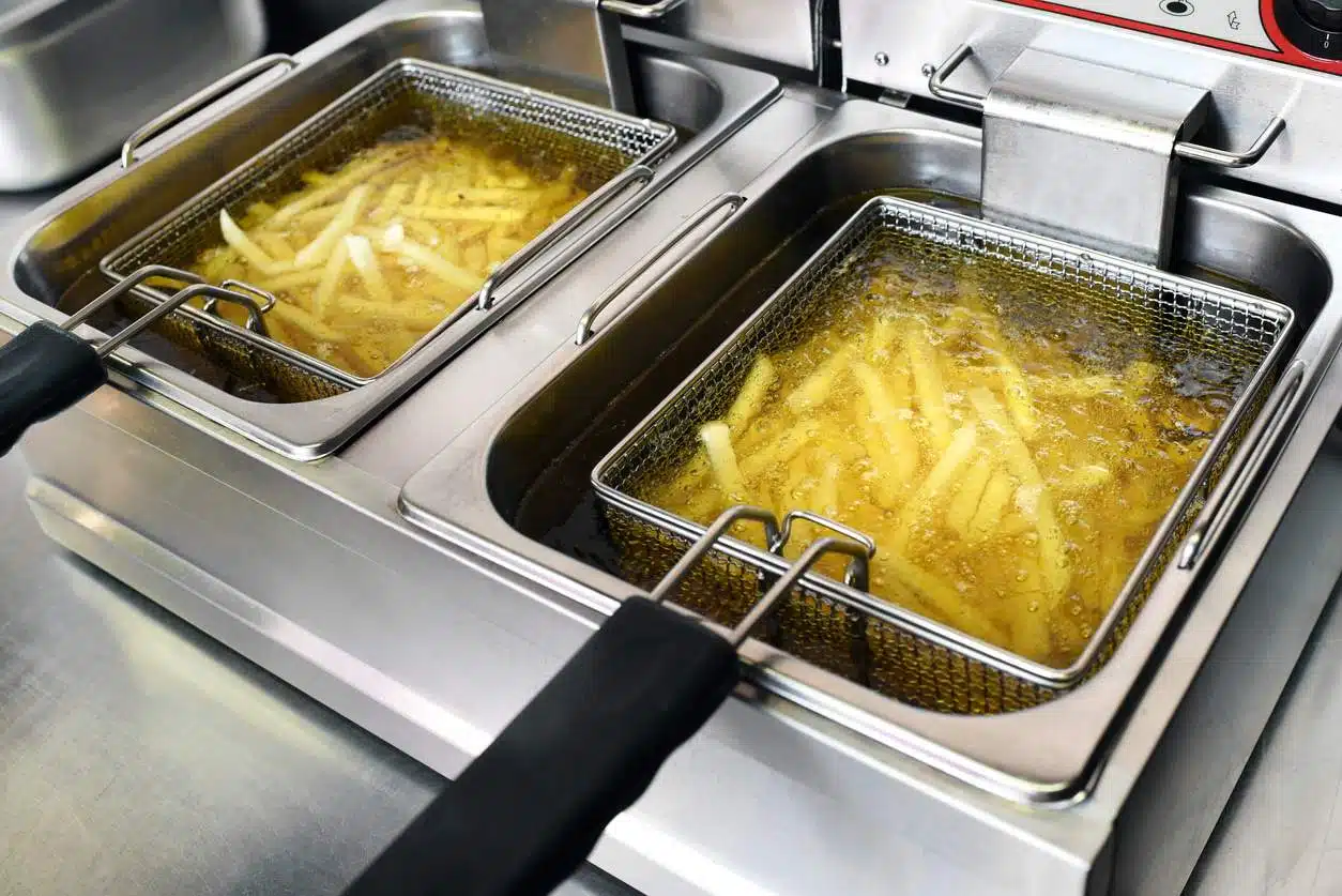 French fries or potato chips deep frying in oil in a commercial metal fryer in a restaurant
